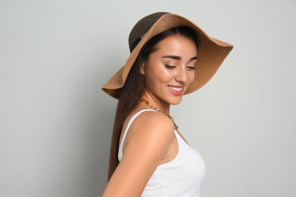 Beautiful young woman wearing straw hat on light grey background. Stylish headdress - Foto, immagini
