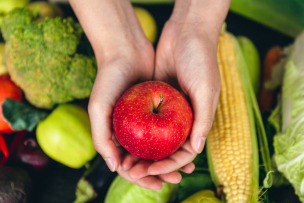 野菜を背景に、女性の手にリンゴ、栄養と健康の概念をクローズアップ. - 写真・画像