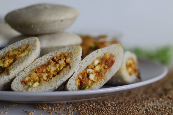 Paneer stuffed kodo millet Idly. Steamed savory cakes made of kodo millets and lentil flour stuffed with a patty made of scrambled cottage cheese with onions and tomatos. Shot on white background - Photo, Image