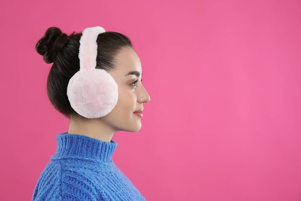 Beautiful young woman wearing earmuffs on pink background. Space for text - Фото, зображення