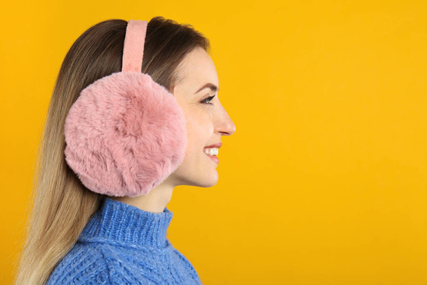 Happy woman wearing warm earmuffs on yellow background, space for text - Foto, Bild
