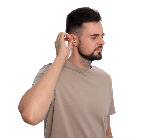 Young man cleaning ear with cotton swab on white background - Foto, afbeelding