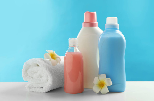 Bottles of laundry detergents, towel and plumeria flowers on white table - Foto, Bild