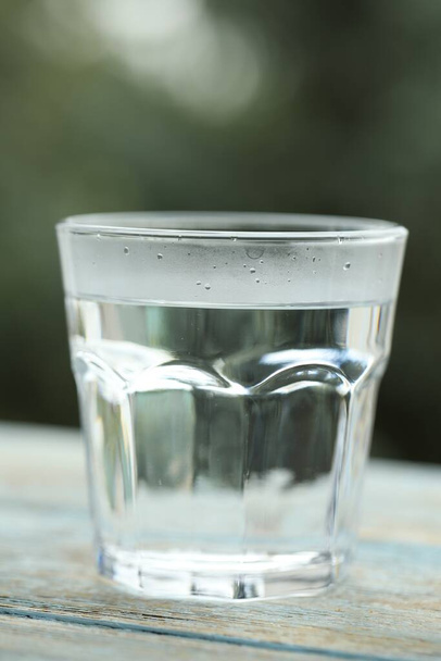 Glass of pure water on light blue wooden table against blurred background, closeup - Foto, afbeelding