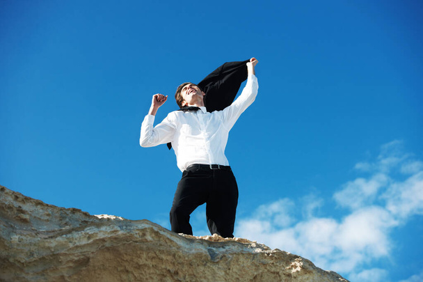 Liberarse de la rutina de 9 a 5. Vista de bajo ángulo del hombre de negocios feliz de pie sobre una roca con las manos en el aire en un gesto de victoria - Foto, Imagen