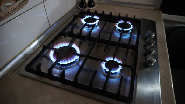 A blue fire is burning on the gas stove. Gas at home. Metal gas stove. Black bars. Light switches of burners. The gas is working. Beige tiles on the walls. Stop the economic crisis. Warmth in house - Photo, Image