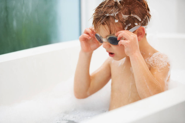 ik ga onder... een schattige jonge jongen zit in het bad zijn bril aan te passen - Foto, afbeelding