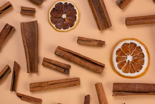 background with cinnamon sticks and dried lemon or orange slices on a beige background, cozy food, spicy trendy background. - Foto, imagen