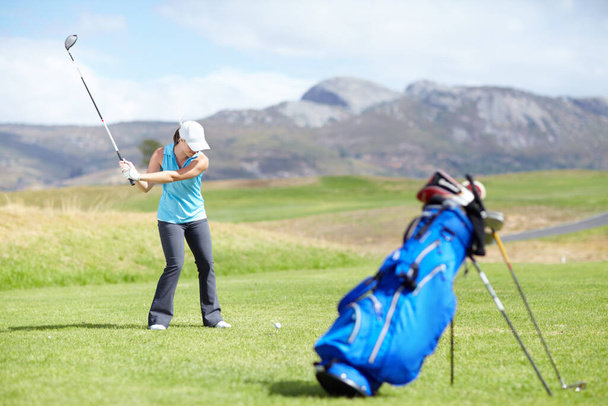 Megcsináljuk a vágást. Egy női golfozó készül lőni egy homályos golftáskával az előtérben. - Fotó, kép