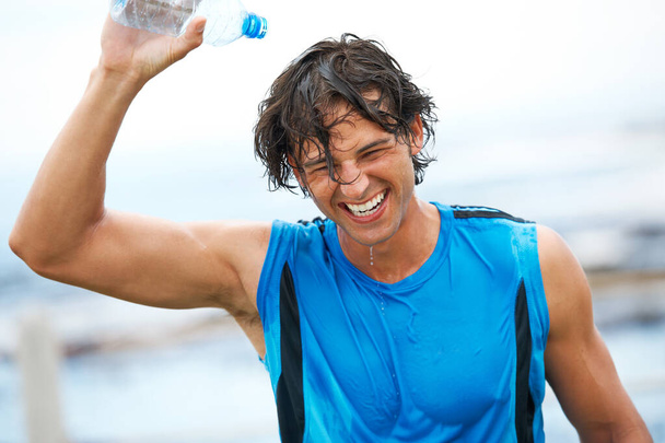 A hard workout feels great. An ecstatic young male laughing and pouring cold water over his head after an intense training session - Fotografie, Obrázek