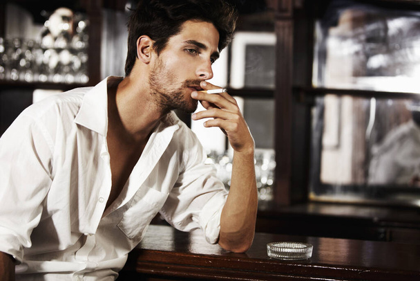 Smoldering with sophistication. A handsome young man smoking at the bar - Zdjęcie, obraz