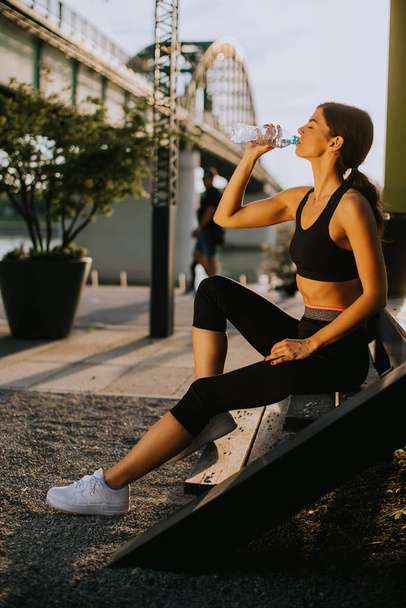 Взгляд на молодую женщину, делающую перерыв во время прогулки на свежем воздухе и пьющую воду - Фото, изображение