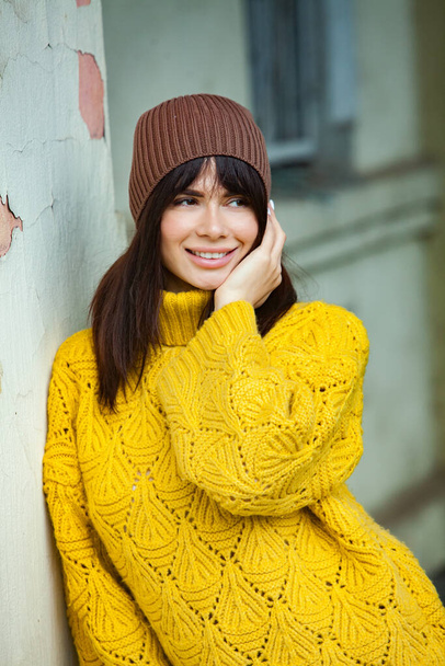 Hermosa morena europea vestida con un suéter de lana amarilla y sombrero afuera. La hermosa chica que usa ropa gruesa y elegante de otoño en tiempo fresco. - Foto, imagen