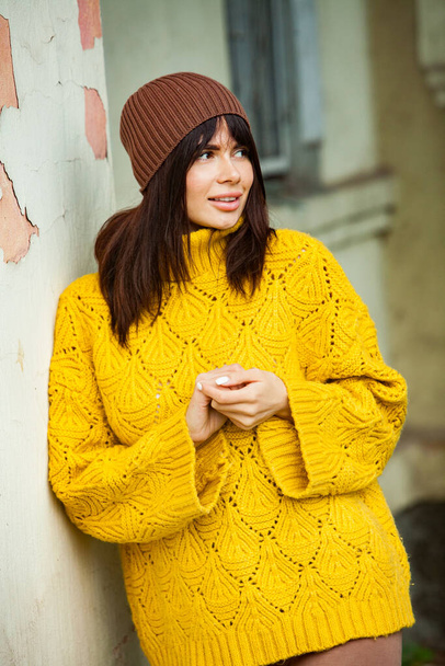 Gyönyörű európai barna ruhás, sárga gyapjú pulóver és kalap kívül. A gyönyörű lány, aki vastag, stílusos őszi ruhákat hord hűvös időben. - Fotó, kép