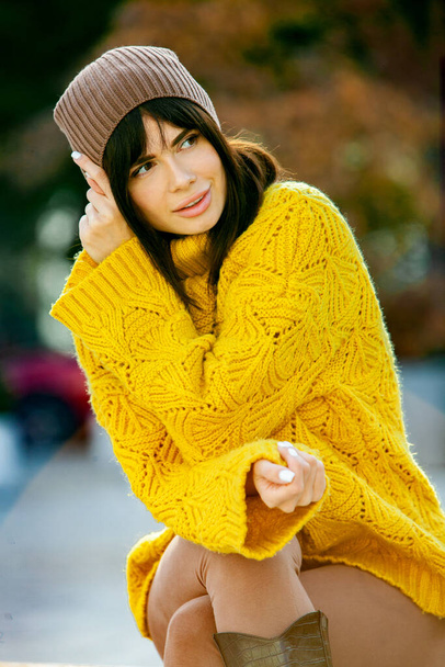 Mooie Europese brunette gekleed in een gele wollen trui en hoed buiten. Het mooie meisje dat dikke stijlvolle herfstkleding draagt bij koel weer. - Foto, afbeelding