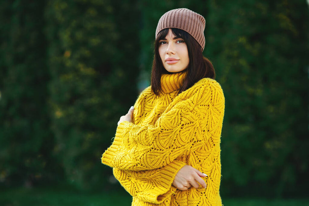Bella bruna europea vestita con un maglione e un cappello di lana gialli all'esterno. La bella ragazza che indossa spessi vestiti eleganti autunno nel bel tempo. - Foto, immagini