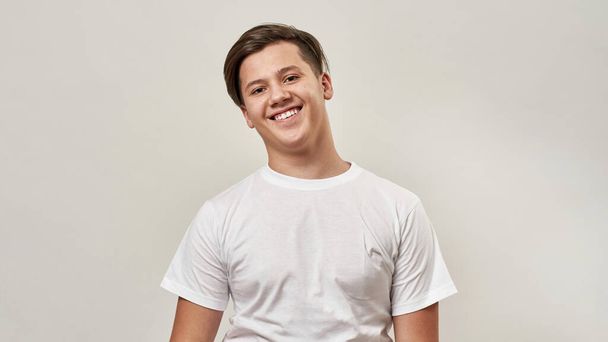 Partial image of smiling european teenage boy looking at camera. Guy of zoomer generation wearing t-shirt. Concept of modern youngster lifestyle. Isolated on white background. Studio shoot. Copy space - Photo, image