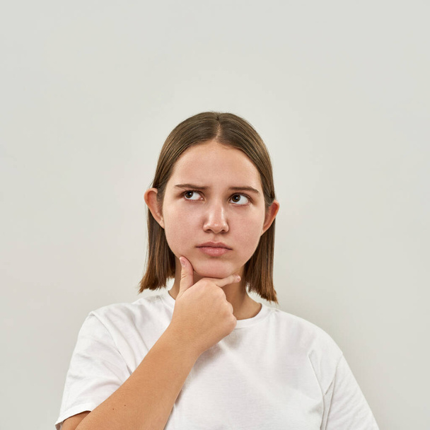 Partial image of caucasian teenage girl thinking about something. Female of zoomer generation wearing t-shirt. Concept of modern youngster lifestyle. Isolated on white background in studio. Copy space - Фото, зображення