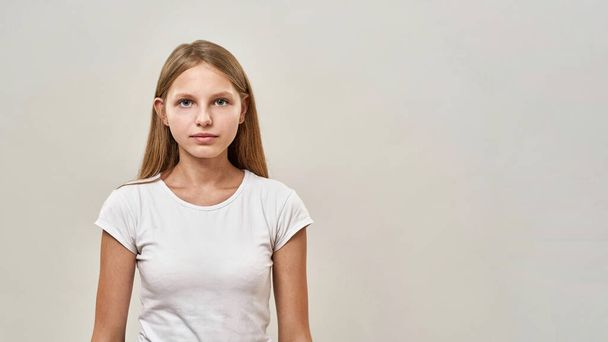 Cropped image of serious caucasian teenage girl looking at camera. Female child of zoomer generation. Concept of modern youngster lifestyle. Isolated on white background. Studio shoot. Copy space - Foto, imagen
