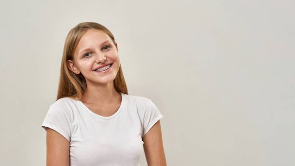 Partial image of smiling caucasian teenage girl looking at camera. Female child with braces of zoomer generation. Modern youngster lifestyle. Isolated on white background. Studio shoot. Copy space - Valokuva, kuva