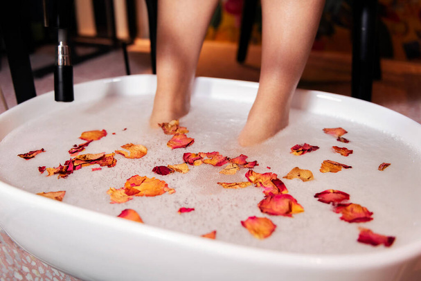 female feet soaking in a bucket with a water and flower petals bath for a pedicure, concept of wellness and body care - Photo, Image