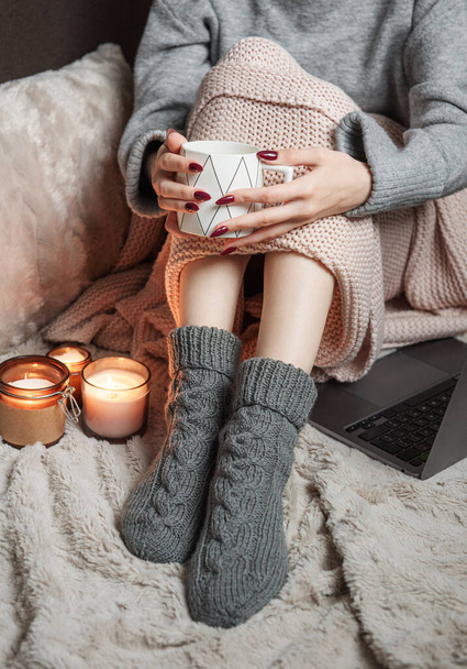 Gemütlich zu Hause, Frau mit warmer Decke bedeckt, trinkt Kaffee und arbeitet an einem Laptop. Entspannen, unbeschwert, komfortabler Lebensstil. - Foto, Bild