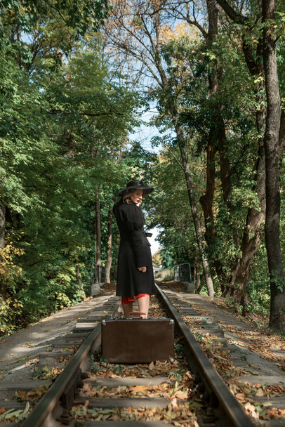 A fekete kabátos nő a síneken hagyta a bőröndöt, és elmegy. Őszi erdő. - Fotó, kép