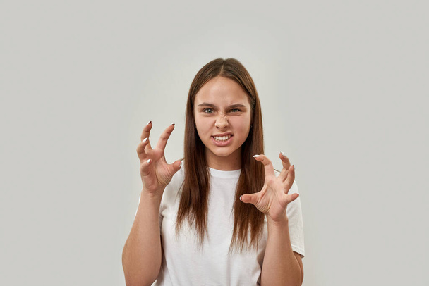 Front view of angry caucasian female teenage posing like ghost while gesticulating with hands. Girl of zoomer generation. Modern youngster lifestyle. White background. Studio shoot. Copy space - Photo, image