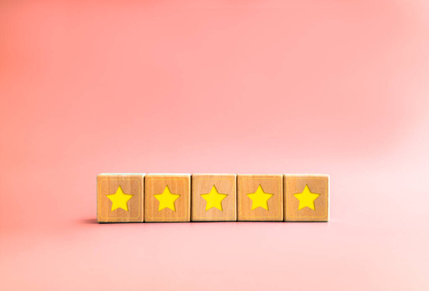 Client feedback survey with yellow star on five wooden cube blocks on pastel pink background with copy space, minimal style. Five stars customer product rating review. Client experience satisfaction. - Photo, Image