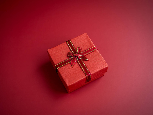Una pequeña caja regalo regalo rojo con cinta sobre fondo rojo, vista superior. Un regalo esencial en días especiales, cumpleaños, Año Nuevo, San Valentín y aniversarios. - Foto, imagen