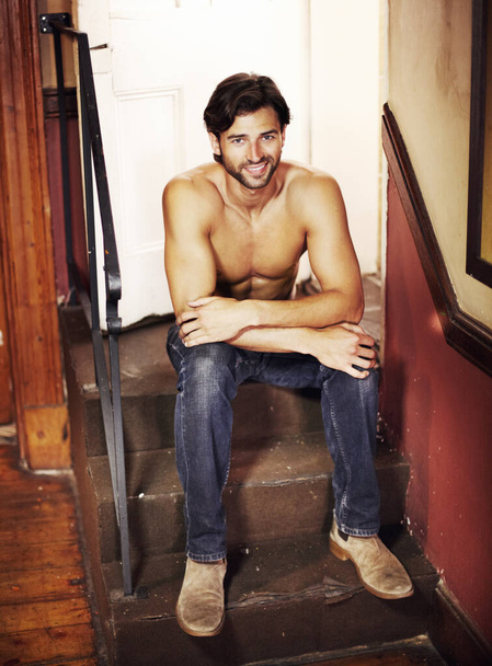 Keeping it casual and sexy. Handsome young man without a shirt on sitting on stairs smiling at you - Foto, afbeelding