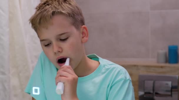 Сонний школяр чистить зуби у ванній перед дзеркалом. Втомлений хлопчик проводить ранкові гігієнічні процедури
. - Кадри, відео