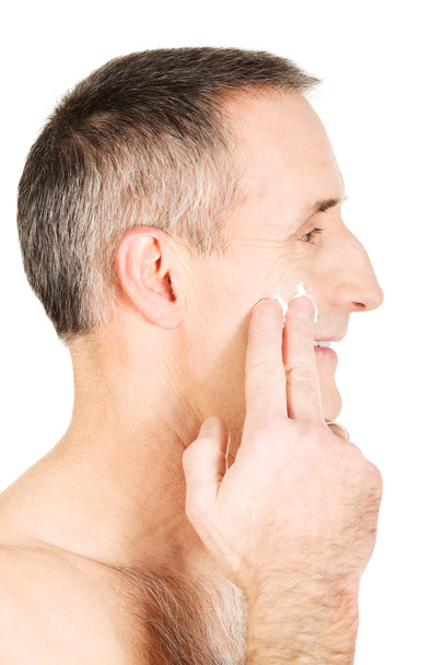Side view of a man applying cream on his face - 写真・画像