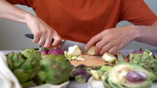 Cerrar Hombre con cuchillo cortando alcachofa en tabla de cortar de madera en la mesa. Cocinar Alimentos saludables y alcachofas de verduras en rodajas.  - Imágenes, Vídeo