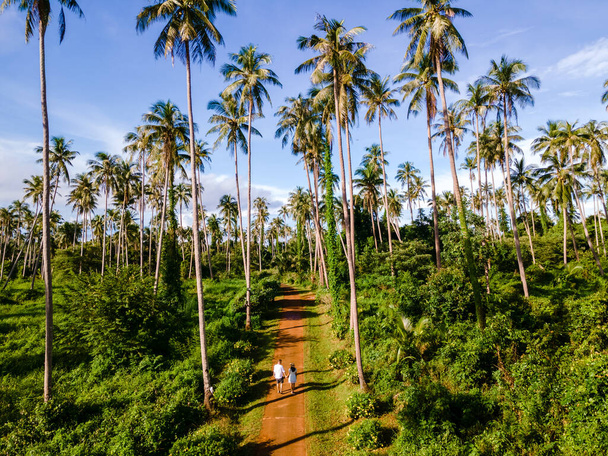 mężczyzn i kobiet spacerujących po drodze między palmami na wyspie Koh Mak Tajlandii. ogromne palmy na tropikalnej wyspie Koh Mak - Zdjęcie, obraz