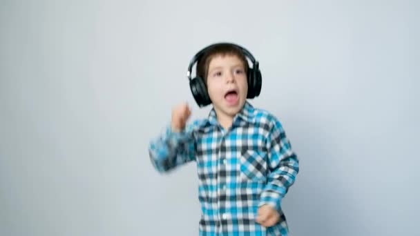 Un niño de 5 años con auriculares salta con las manos en alto sobre un fondo blanco - Metraje, vídeo