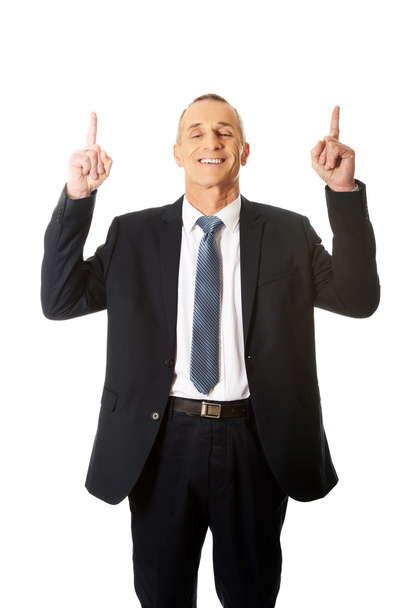 Businessman pointing upwards and smiling at camera - Foto, Bild