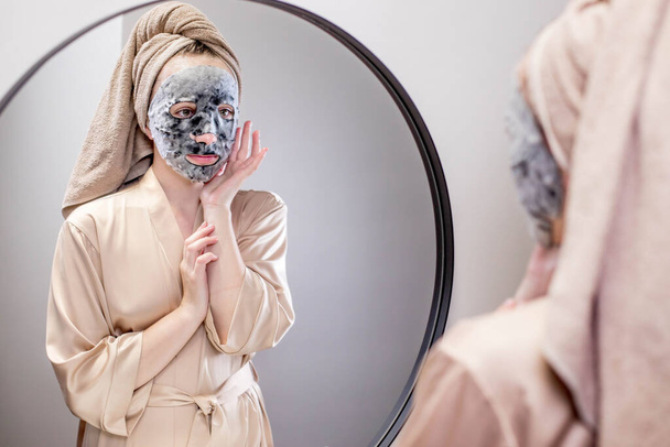 Mujer joven aplicando mascarilla en el baño y sonriendo. Hermosa mujer frente a un espejo haciendo tratamientos de belleza - Foto, Imagen