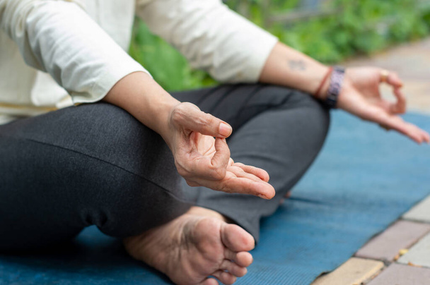 Крупним планом жінка мудра жест руки робить йогу розслаблюючою в позі лотоса, сидячи на килимку. на відкритому повітрі. Практикує медитацію в природі. Фотографія тла
. - Фото, зображення