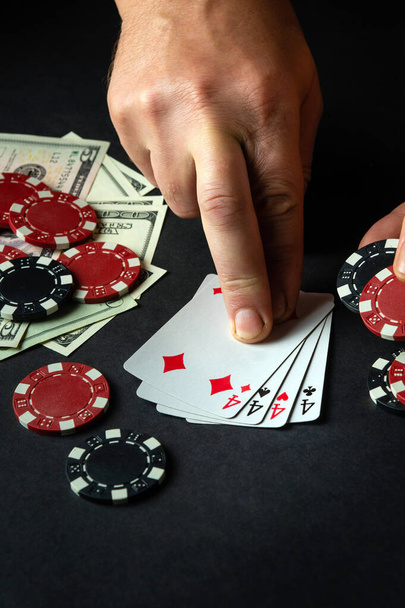 Hráč ukazuje prstem na vítěznou čtyři druhu nebo čtyřkolky kombinace v pokeru na černém stole s žetony a penězi v kasinu. - Fotografie, Obrázek