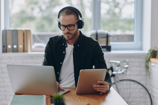 Concentrated man in headphones using technologies while sitting at his working place in office - Foto, immagini