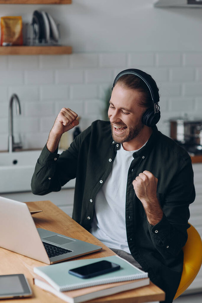 Excited young man in headphones gesturing while looking at laptop - Foto, immagini