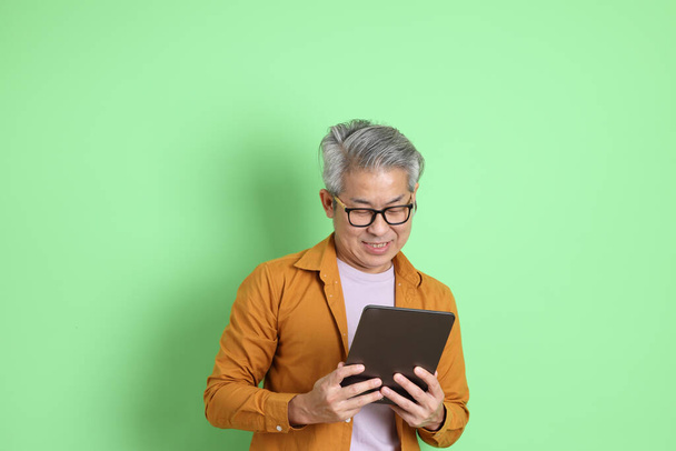 Der erwachsene asiatische Mann der 40er Jahre mit gelbem Hemd steht auf grünem Hintergrund. - Foto, Bild