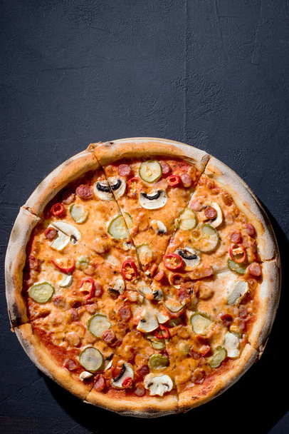Appetizing pizza with hunting sausages, mozzarella cheese, pickled cucumbers, chili peppers on a tomato base. Mexican pizza. Top view. - Photo, Image