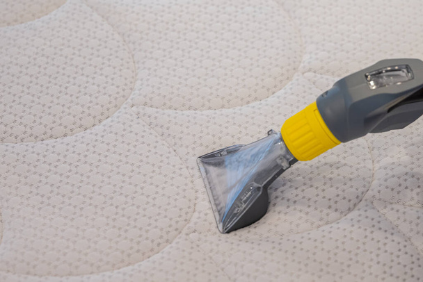 Worker Cleaning a bed with Vacuum Cleaner.Extraction method. - Foto, Bild