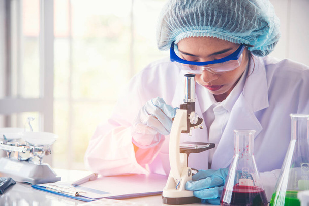 Kobieta naukowiec ręka pisać notatka informacja w medyczny laboratorium patrzeć na nauka mikroskop medyczny test, badawczy biologia chemia. azjatyckie kobiety technik laboratorium analizując badania krwi farmaceutyczne - Zdjęcie, obraz