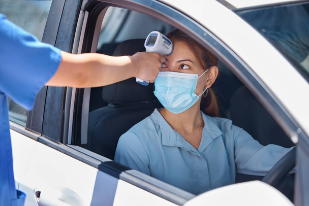 Car, drive thru covid test and thermometer with nurse and patient. Young woman in vehicle, wearing a mask and medical care worker doing fever screening. Masks, coronavirus and testing on site. - 写真・画像