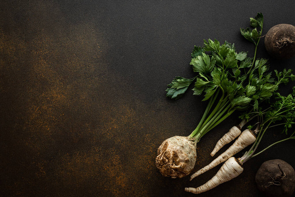Parsley and selera roots with tops and black radish close-up on a brown background, top view, healthy autumn seasonal roots, copy space - Fotó, kép