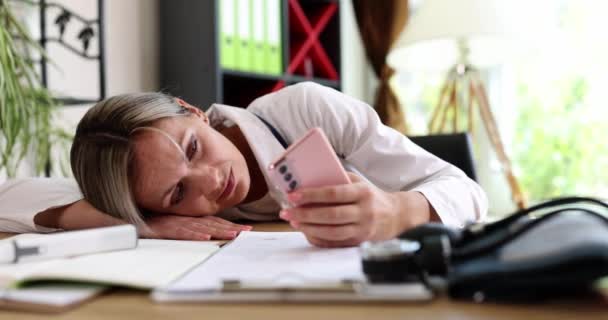 Zmęczona smutna pani doktor patrzy na zbliżenie smartfonów. Zmęczona sfrustrowana kobieta czeka na telefon lub wiadomość - Materiał filmowy, wideo