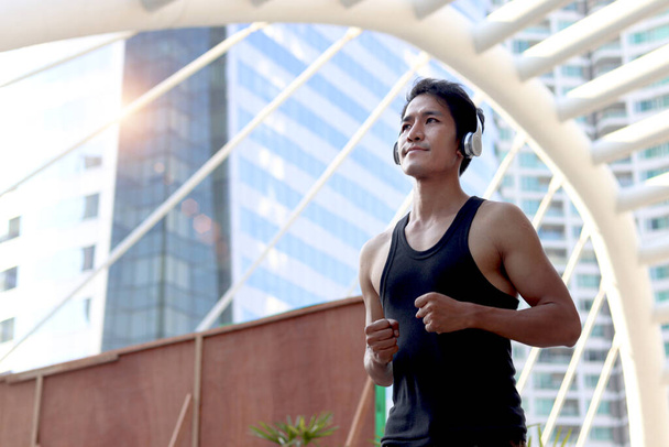 Portrait sport runner handsome man with headphones running outside, exercise run outdoor, male jogger athlete training and doing workout in downtown city.  - Photo, Image